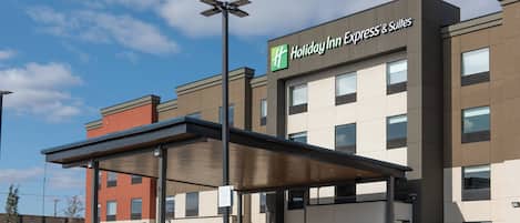 Edificio de Holiday Inn Express & Suites con entrada cubierta, cielo despejado y estacionamiento.