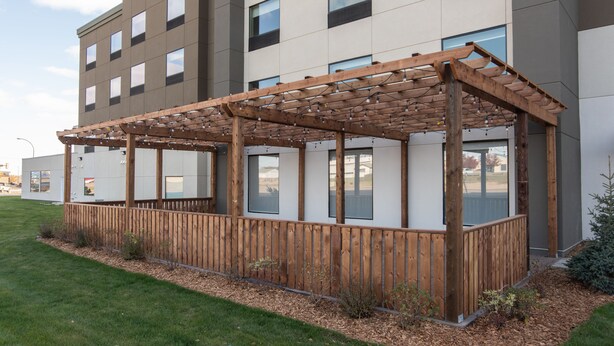 A modern building with a wooden pergola structure, large windows, and a well-maintained lawn. - Holiday Inn Express & Suites North Battleford by IHG (North Battleford)