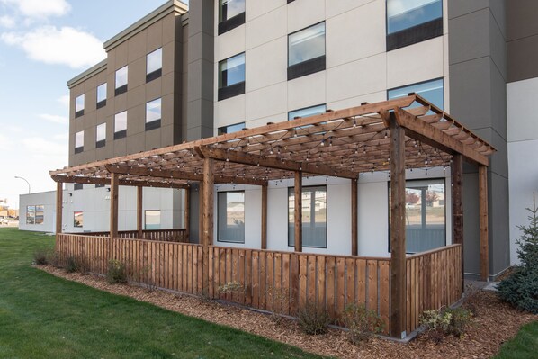 Ein modernes Gebäude mit einer Holz-Pergola, großen Fenstern und einem gepflegten Rasen.