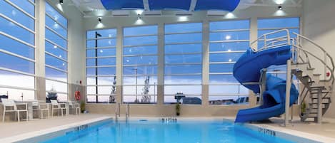 Una piscina con un tobogán azul, ventanas amplias y vistas al cielo.
