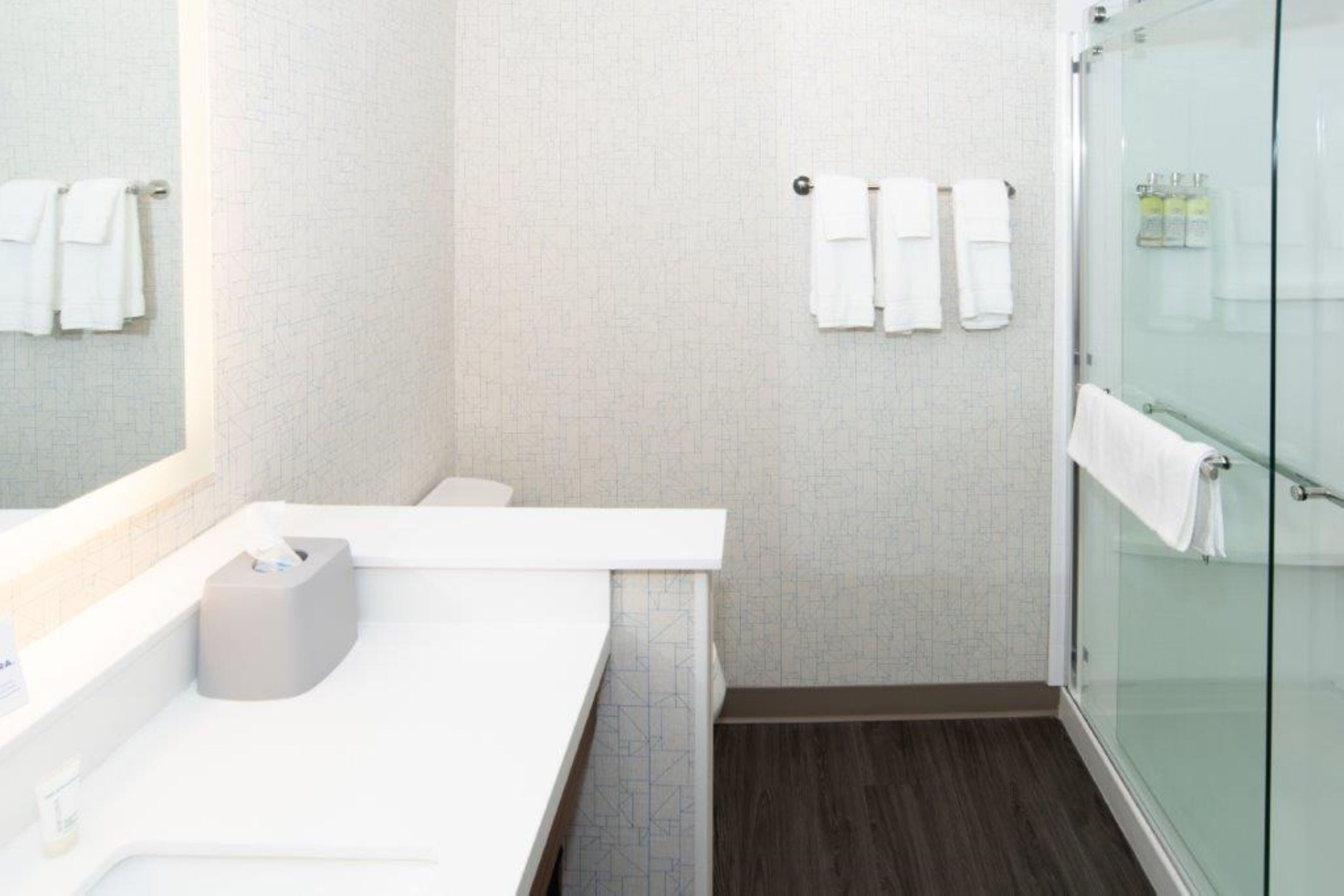 A modern bathroom with a white sink, a glass shower enclosure, and towels hanging on the wall.