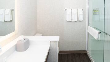 A modern bathroom with a white sink, a glass shower enclosure, and towels hanging on the wall.