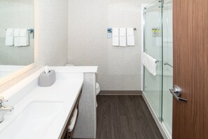 Ein modernes Badezimmer mit einem weißen Waschbecken, einer Duschkabine aus Glas und einer Holztür.