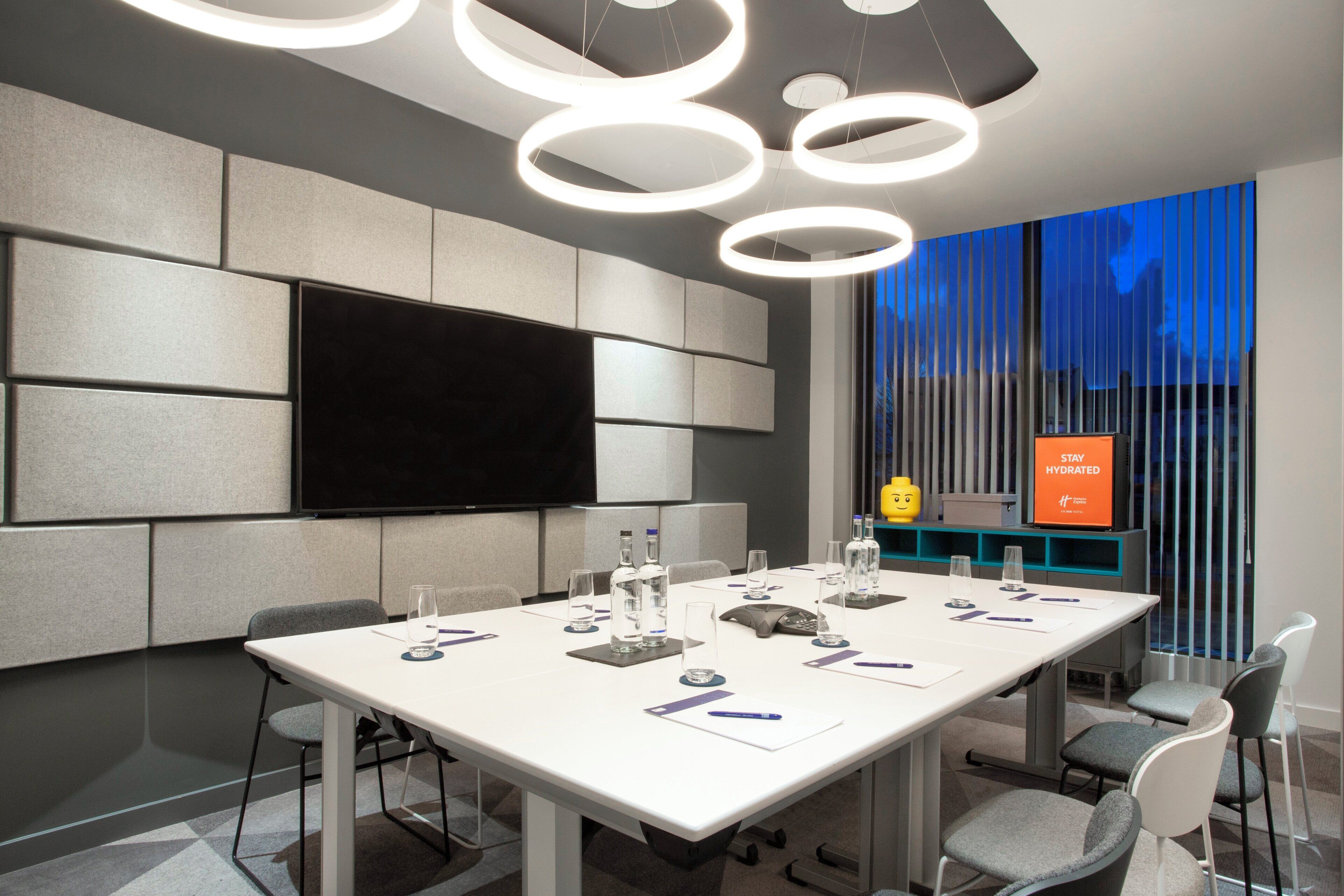 Una sala de conferències amb una gran pantalla plana, una taula blanca i cadires grises.