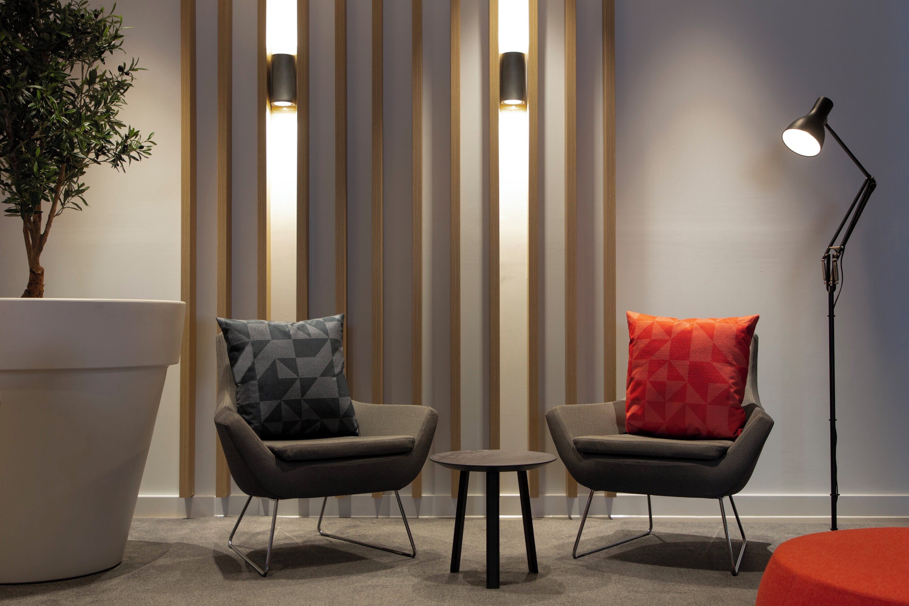 Una habitación moderna con dos sillones, una mesita, una lámpara de pie y una planta grande en maceta.