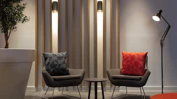 Una habitación moderna con dos sillones, una mesita, una lámpara de pie y una planta grande en maceta.