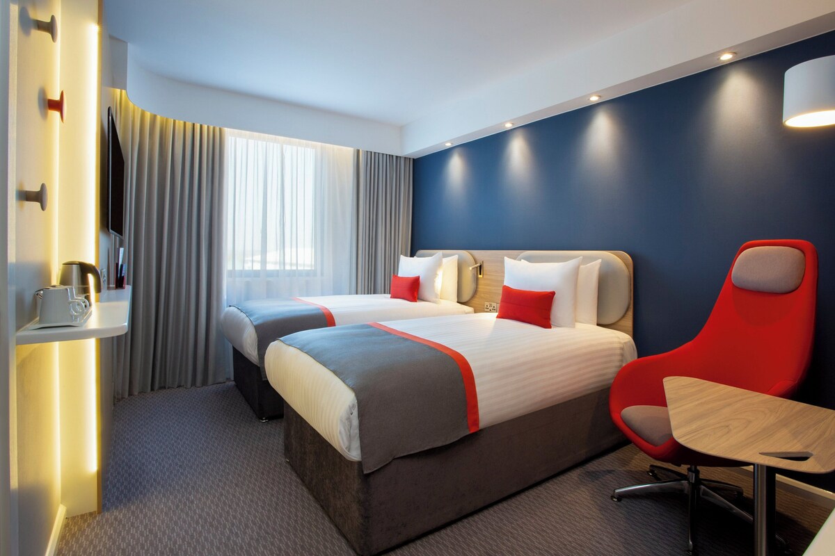 A hotel room with two beds, a red chair, a small table, and a TV.