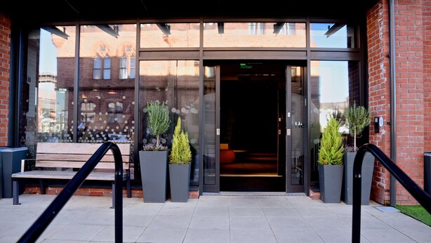 A building entrance with a glass door, a bench, and two potted plants. - Holiday Inn Express Barrow-in-Furness by IHG (Barrow-in-Furness)