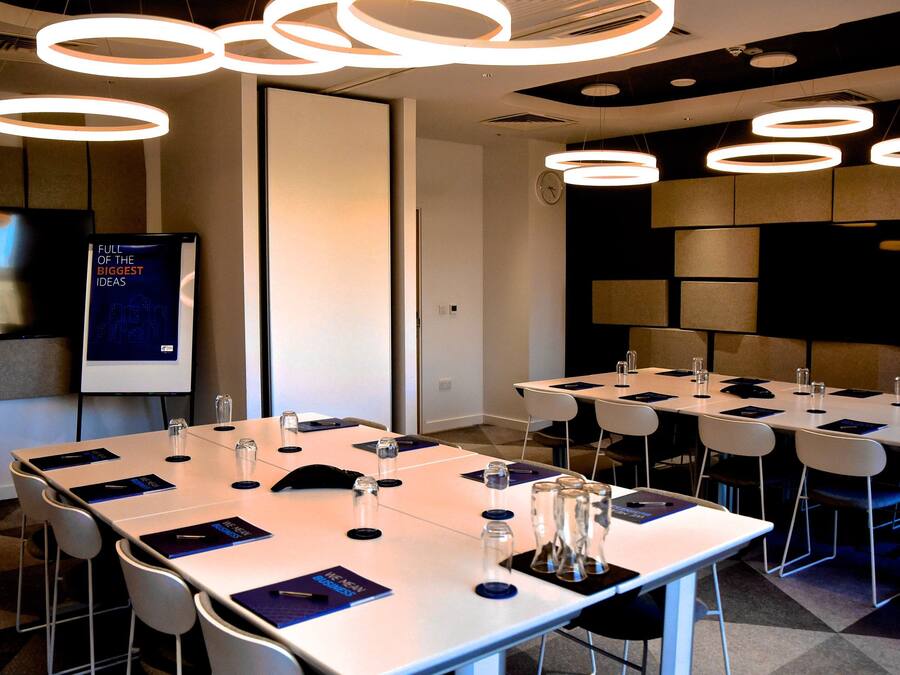 A conference room with multiple tables, chairs, and a large screen displaying a presentation.