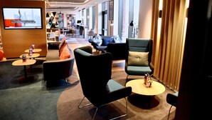 A modern hotel lobby with a mix of seating options including sofas, armchairs, and round tables. There are multiple tables with small items on them, and a television screen is mounted on the wall. - Holiday Inn Express Barrow-in-Furness by IHG (Barrow-in-Furness)
