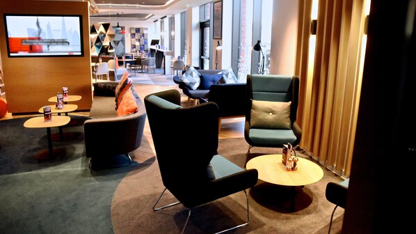 A modern hotel lobby with a mix of seating options including sofas, armchairs, and round tables. There are multiple tables with small items on them, and a television screen is mounted on the wall. - Holiday Inn Express Barrow-in-Furness by IHG (Barrow-in-Furness)