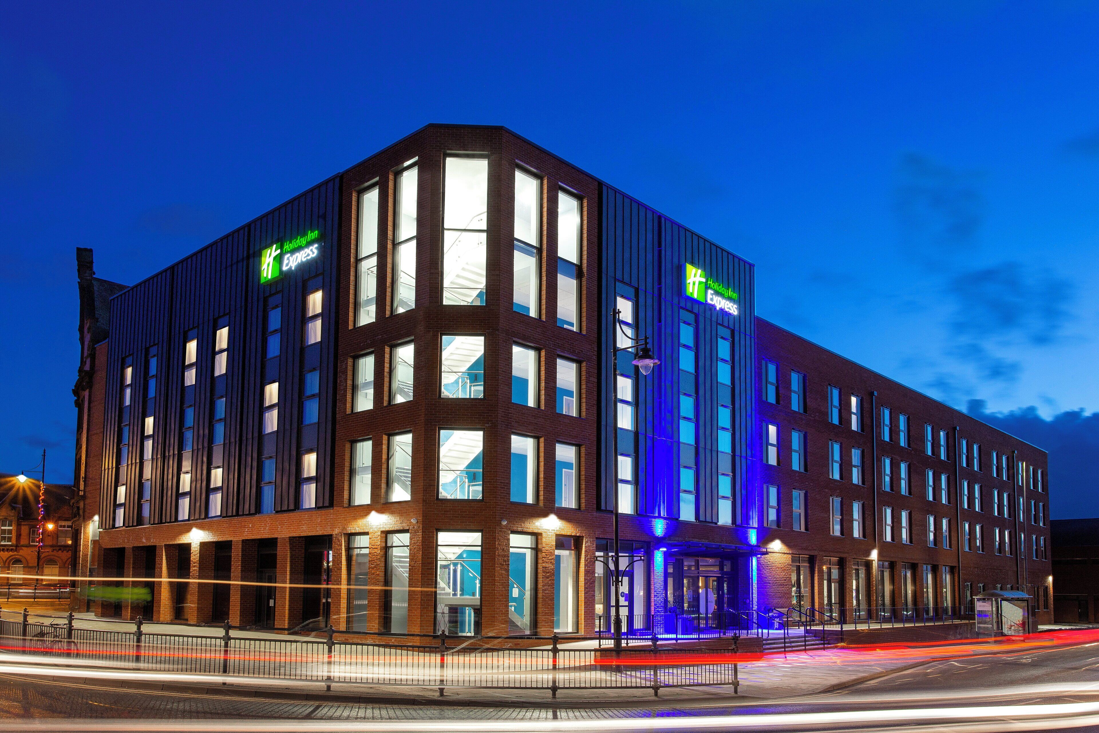A modern hotel with a prominent 'Holiday Inn Express' sign, large windows, and a well-lit entrance.