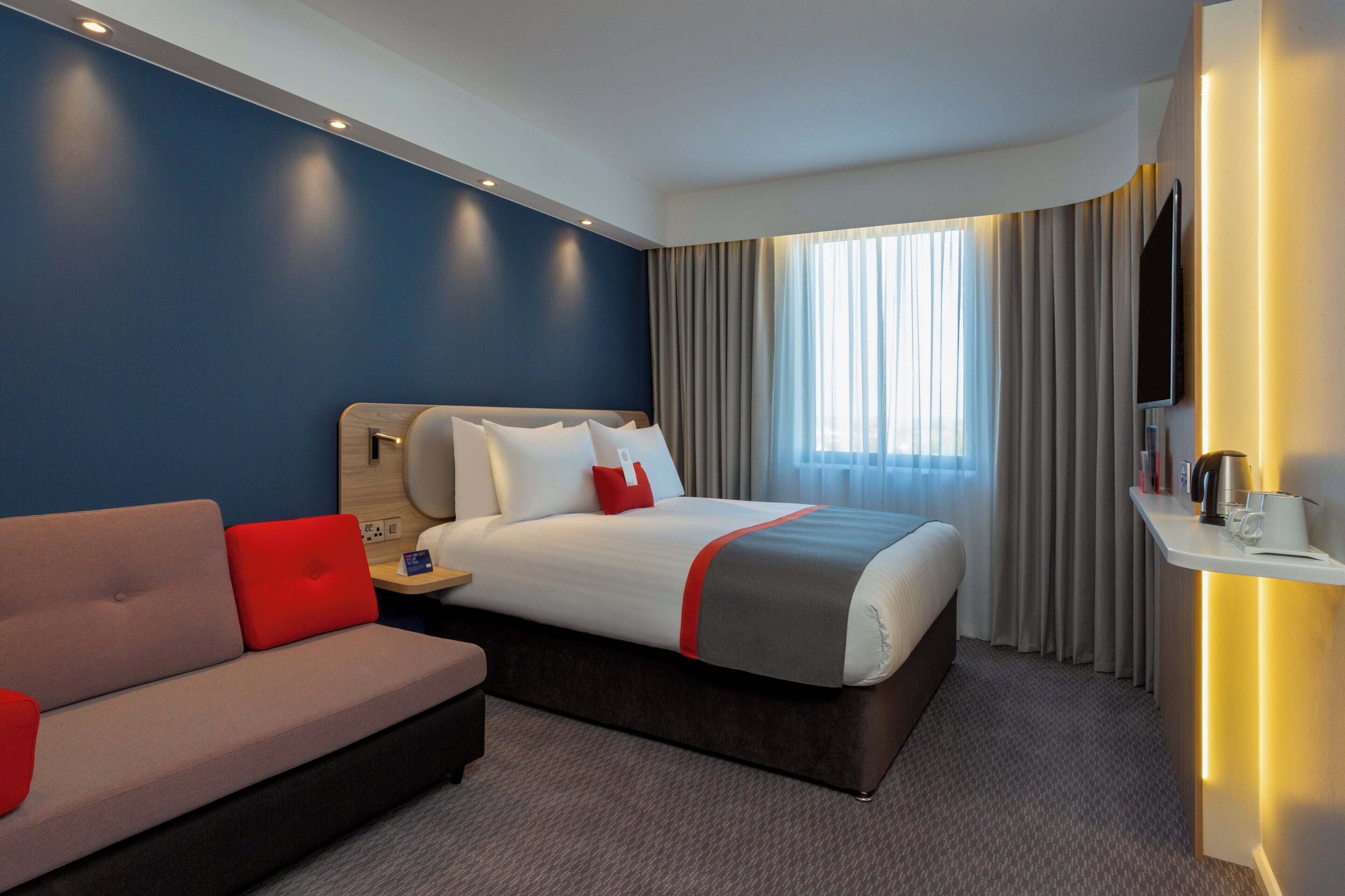 Ein modernes Hotelzimmer mit Bett, Sofa, Fernseher und Nachttisch.