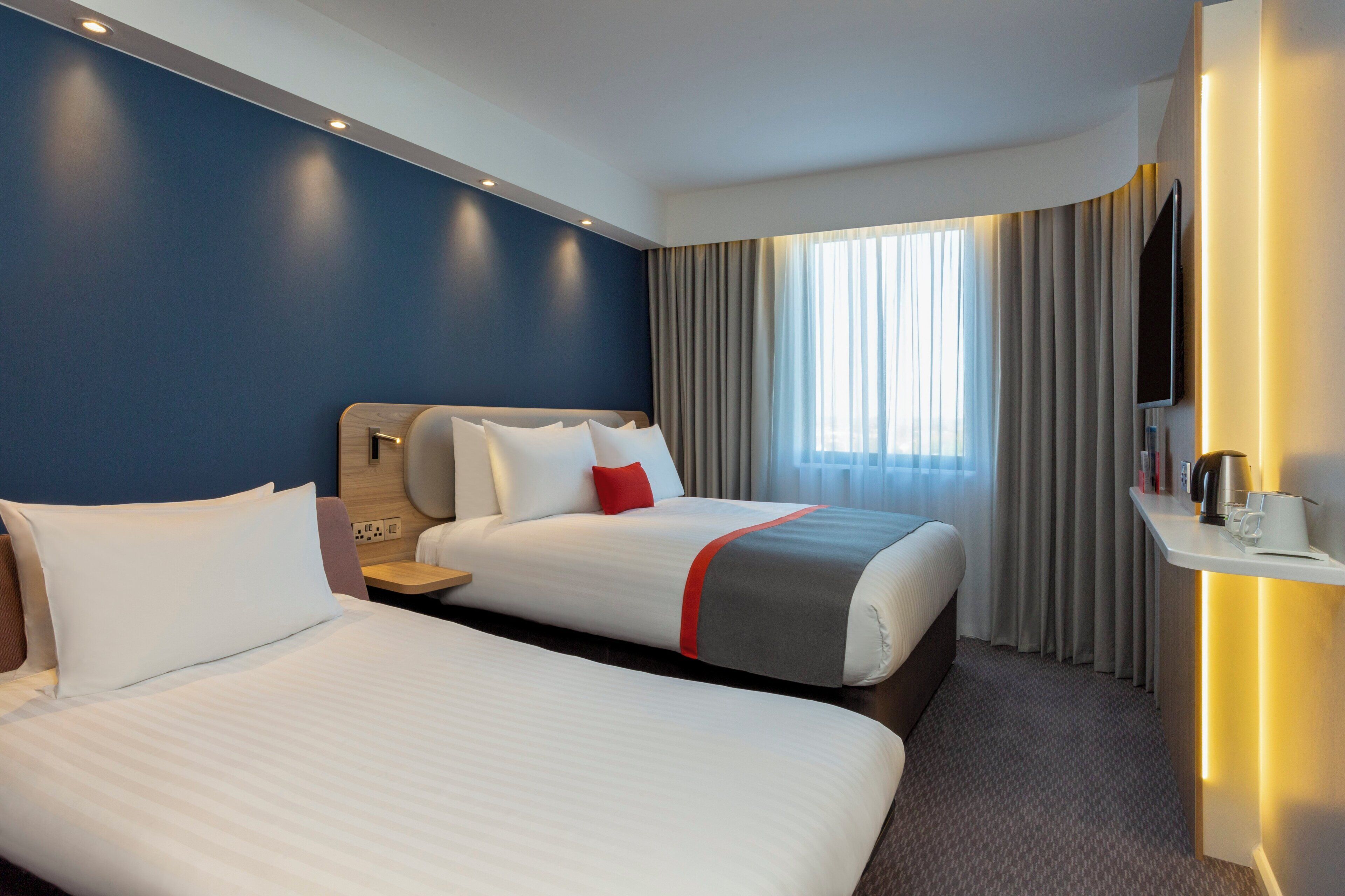 A hotel room with two beds, a TV, a coffee machine, and a window with curtains.