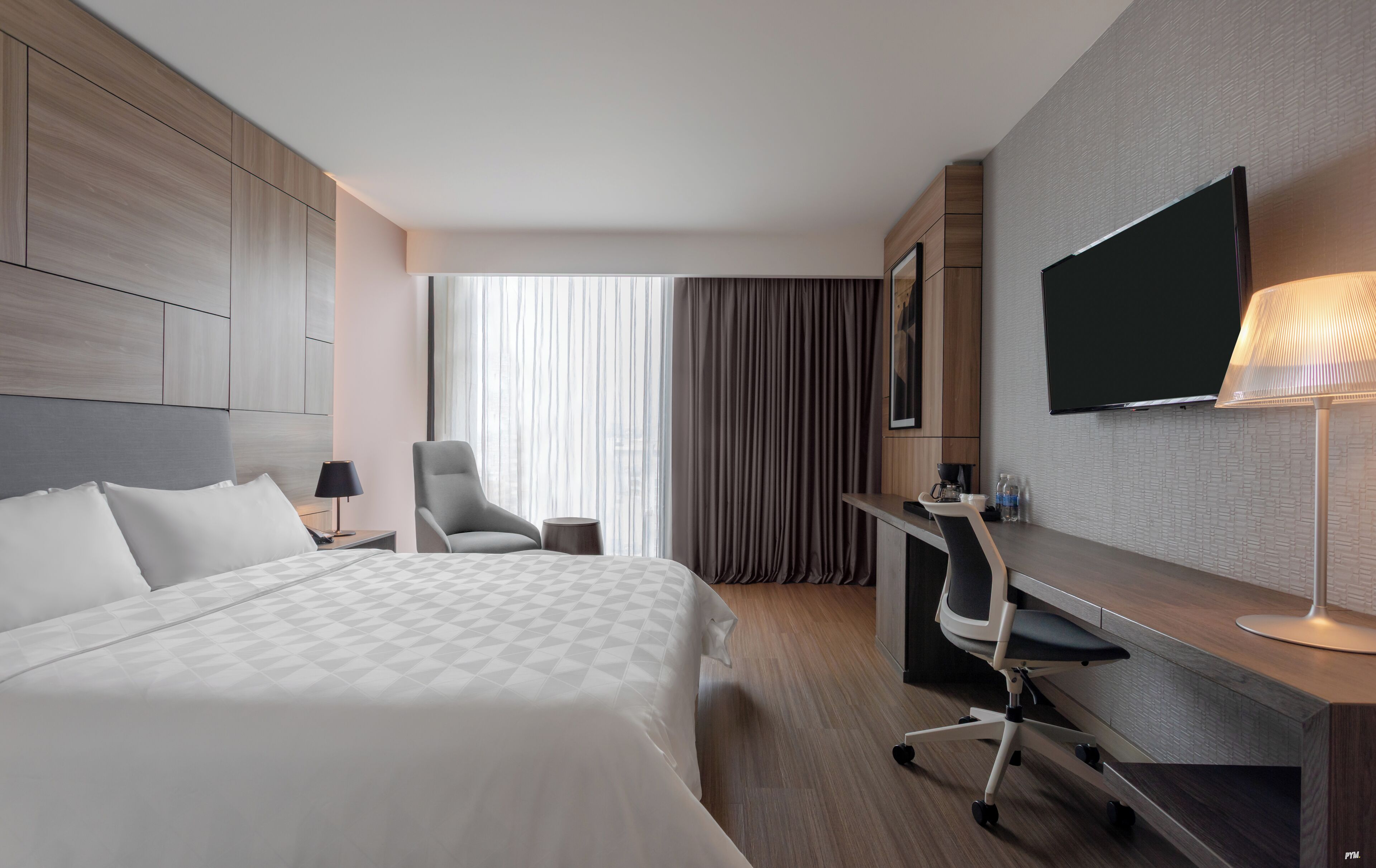 Une chambre d’hôtel avec un lit, un bureau, une chaise, une télévision et une fenêtre avec des rideaux.