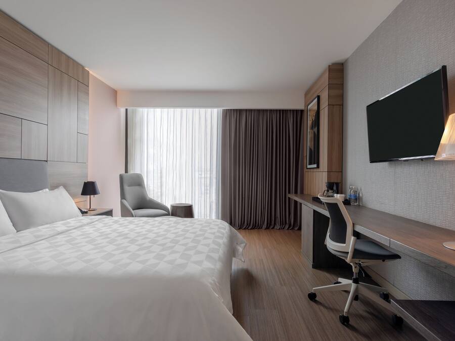 Une chambre d’hôtel avec un lit, un bureau, une chaise, une télévision et une fenêtre avec des rideaux.