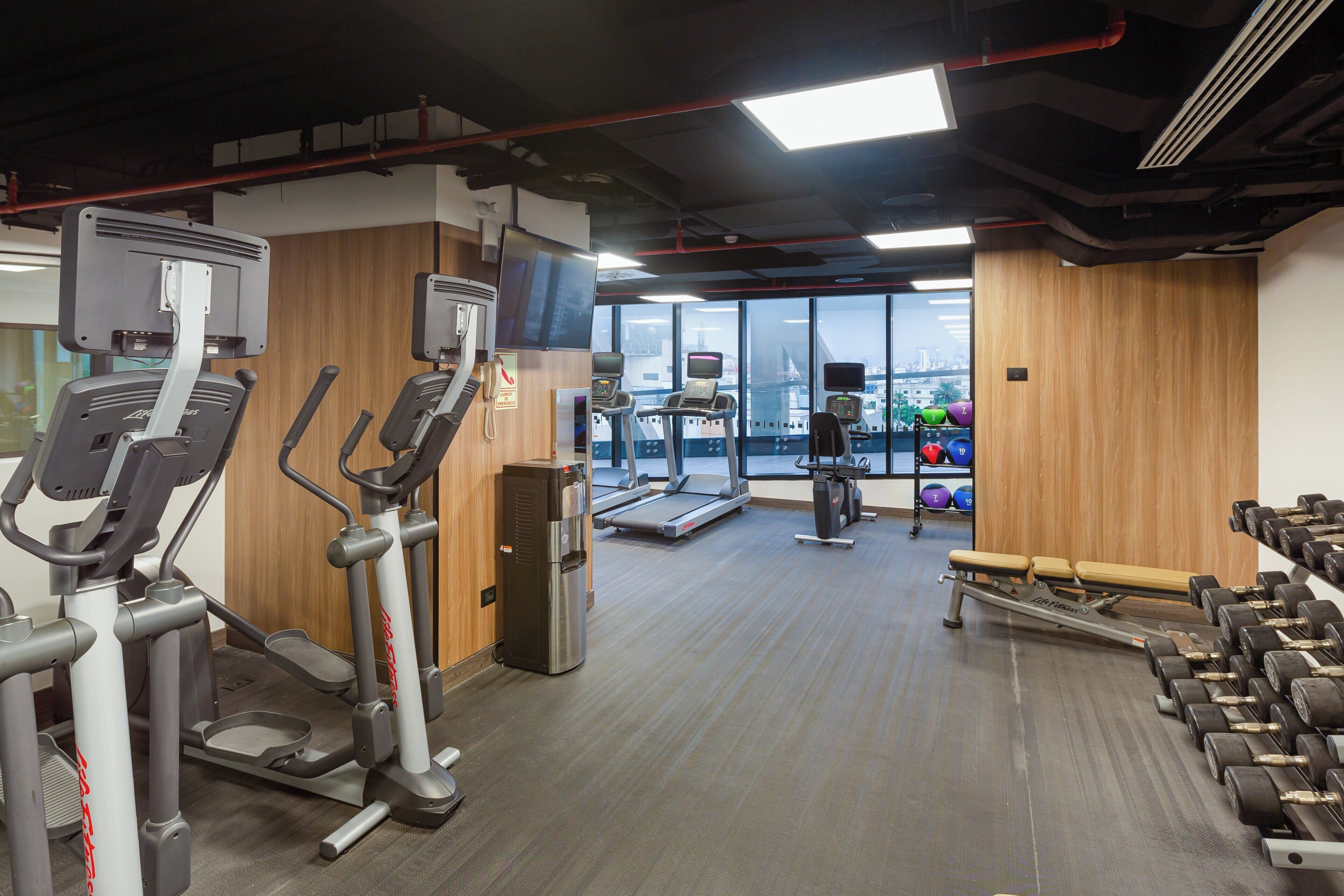 Een fitnessruimte met loopbanden, elliptische trainers, een waterdispenser en gewichten.
