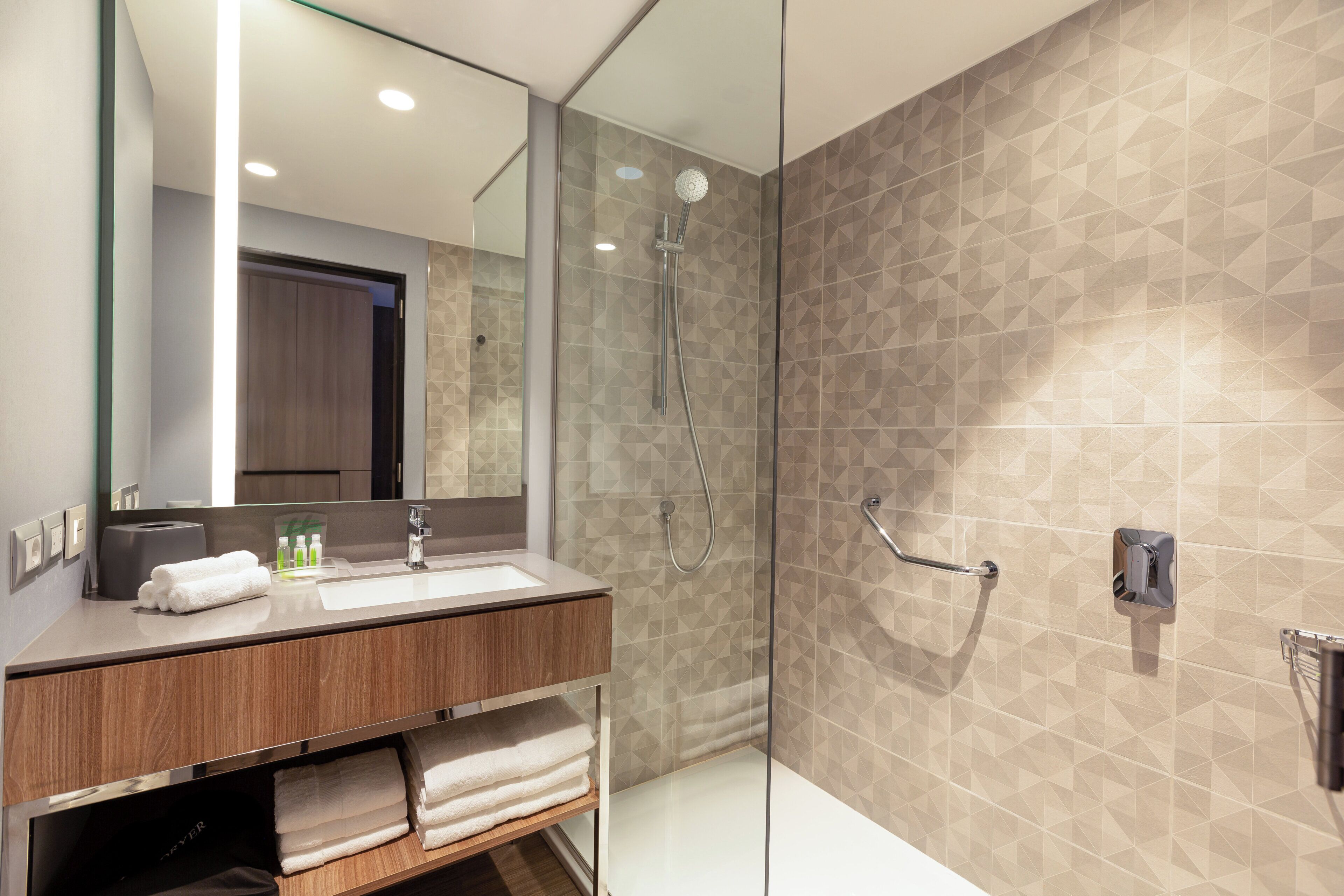 Un baño moderno con ducha de vidrio, tocador de madera con lavamanos y un espejo grande.