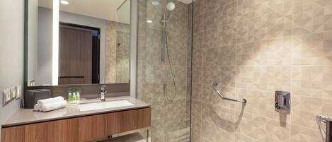 Un baño moderno con ducha de vidrio, tocador de madera con lavamanos y un espejo grande.