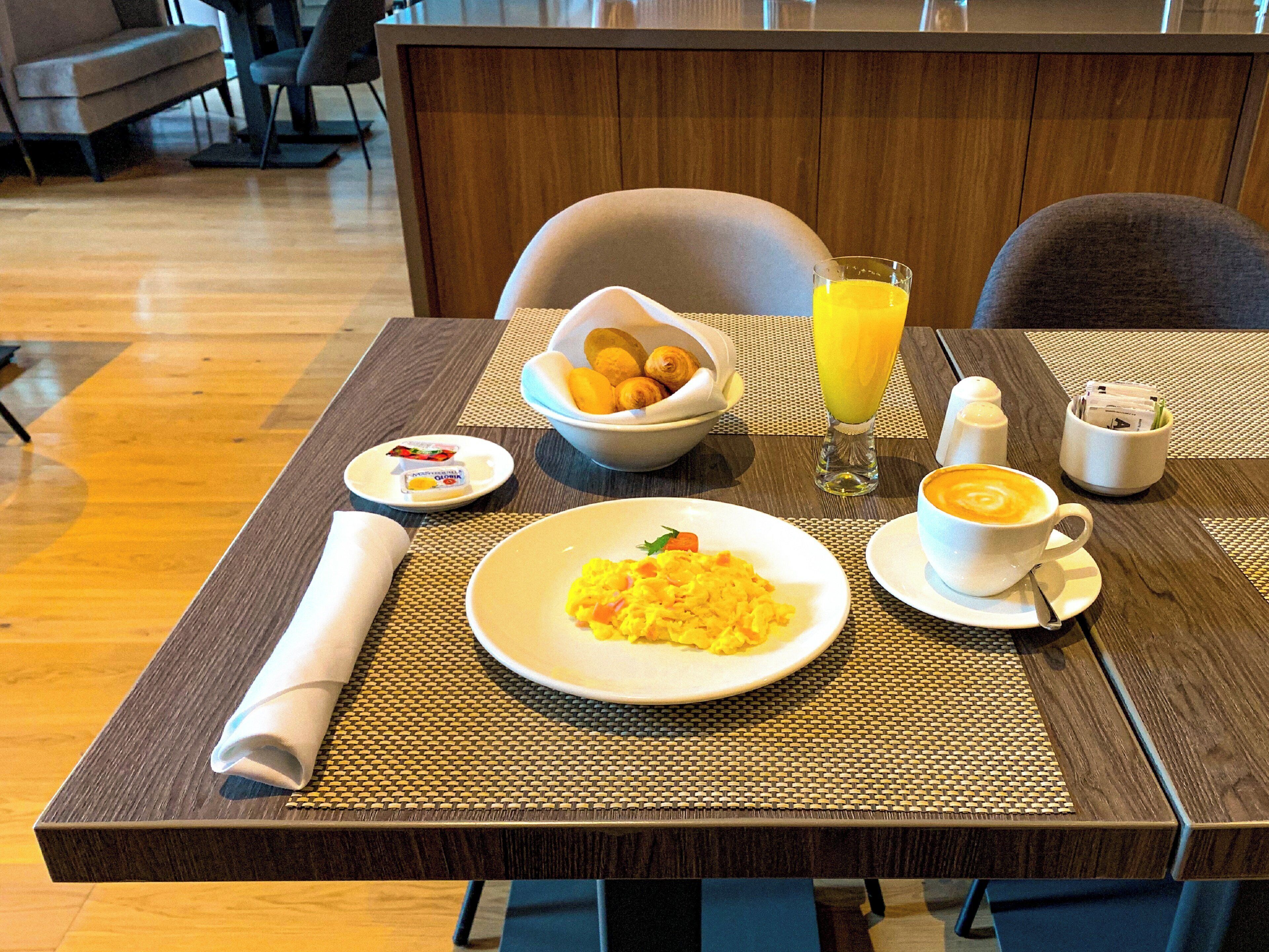 Una mesa de desayuno con platos de comida, un vaso de jugo de naranja y una taza de café.