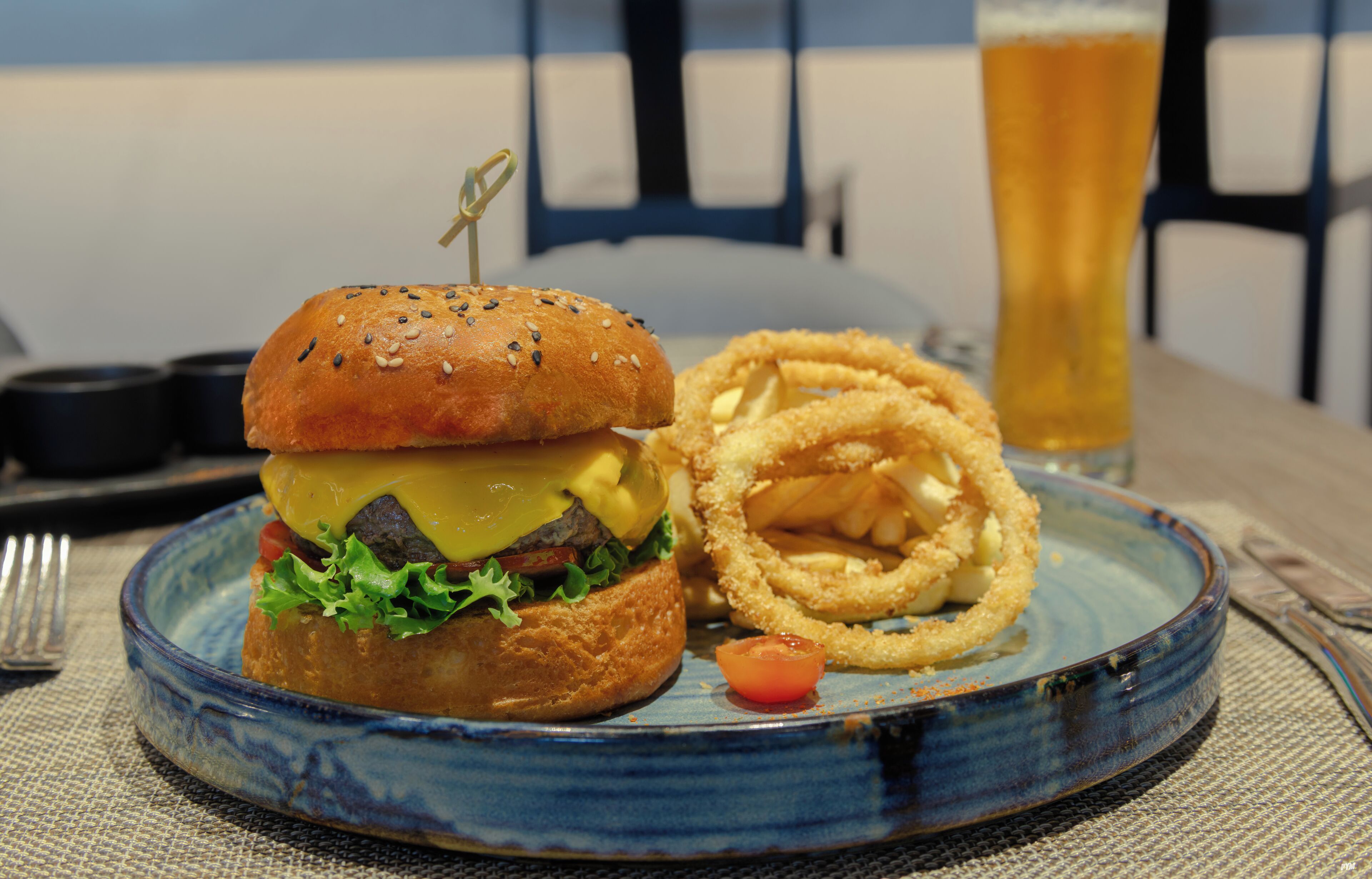 En tallrik med en hamburgare, lökringar och ett glas öl på ett bord.