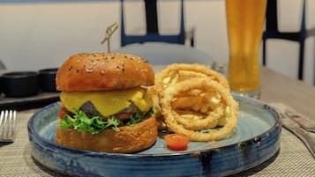 Un plato con una hamburguesa, aros de cebolla y un vaso de cerveza sobre una mesa.