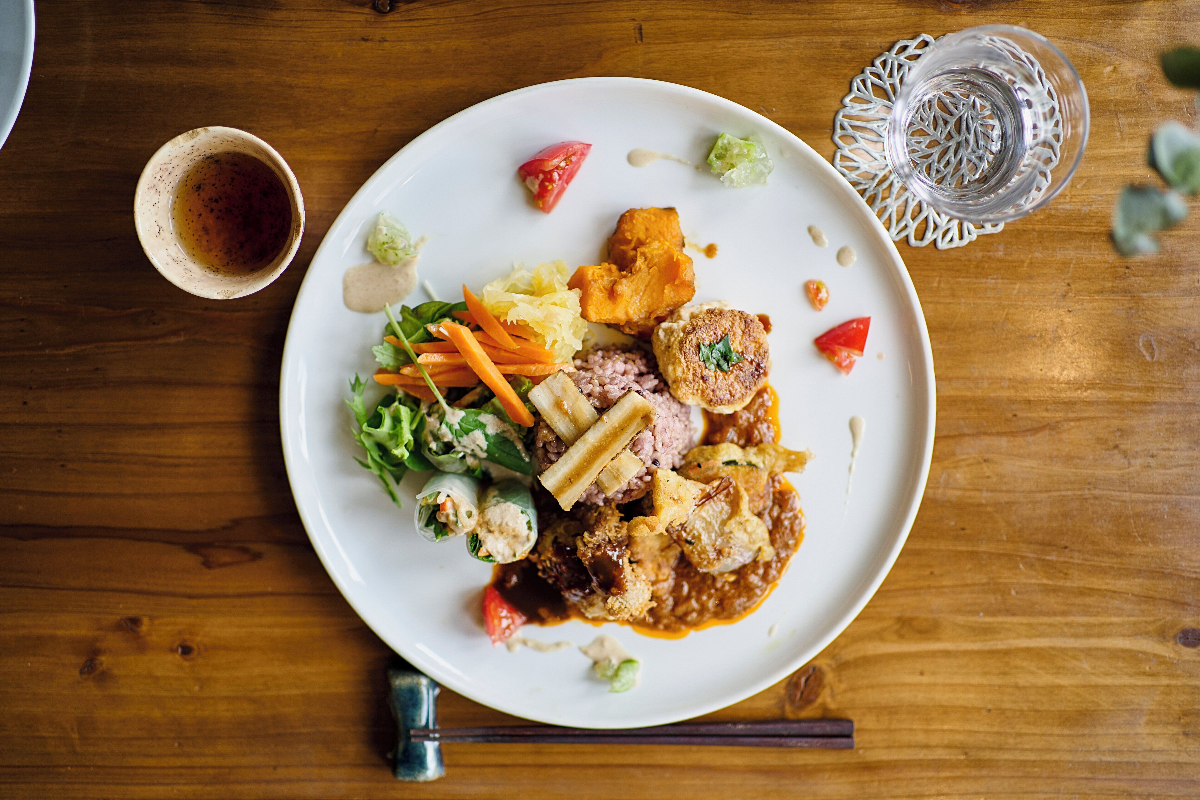 Une assiette remplie de différents aliments, notamment une salade, de la viande et des légumes, posée sur une table en bois.