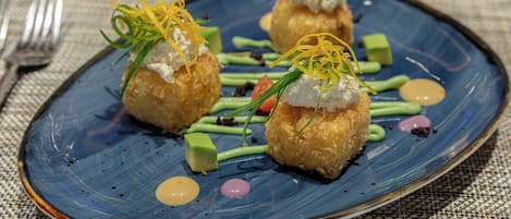 A plate of food with three spherical items topped with a white substance and garnished with green and yellow elements, accompanied by green sauce and small round items.