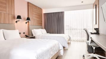 Ein Hotelzimmer mit zwei Betten, einem Schreibtisch mit Stuhl, einem großen Fenster mit Vorhängen und Wandleuchten.
