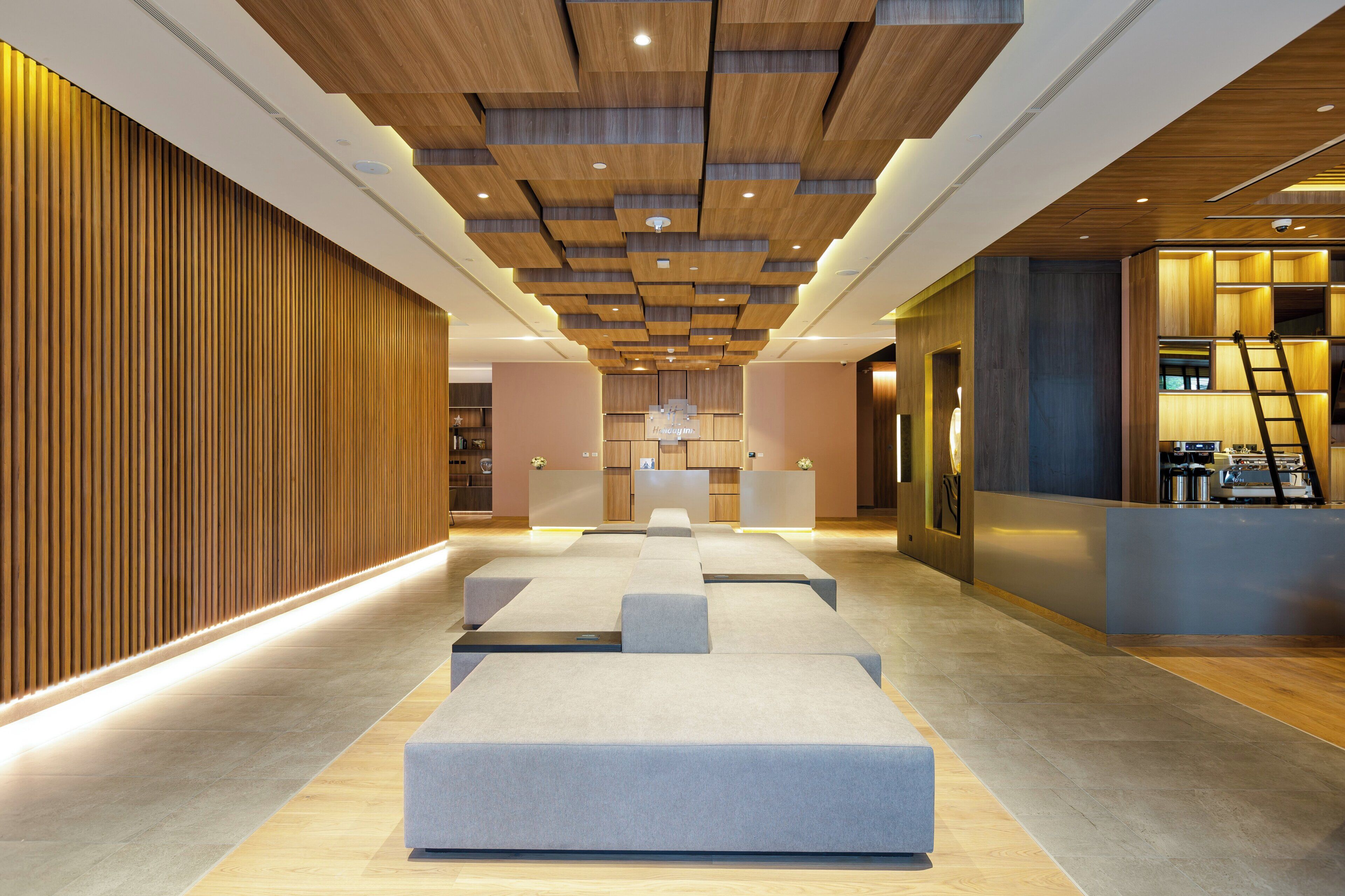 Un moderno vestíbulo de hotel con techo de madera, zona de estar, mostrador de recepción y vista al interior.