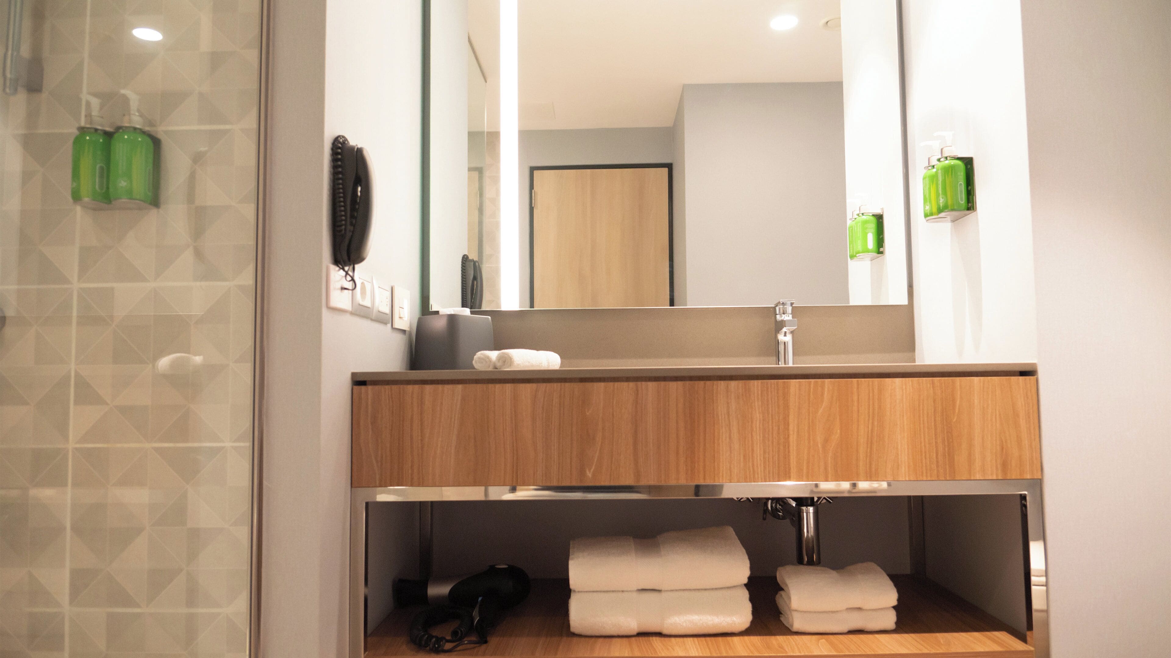 A modern bathroom with a wooden vanity, a large mirror, and a shower area.