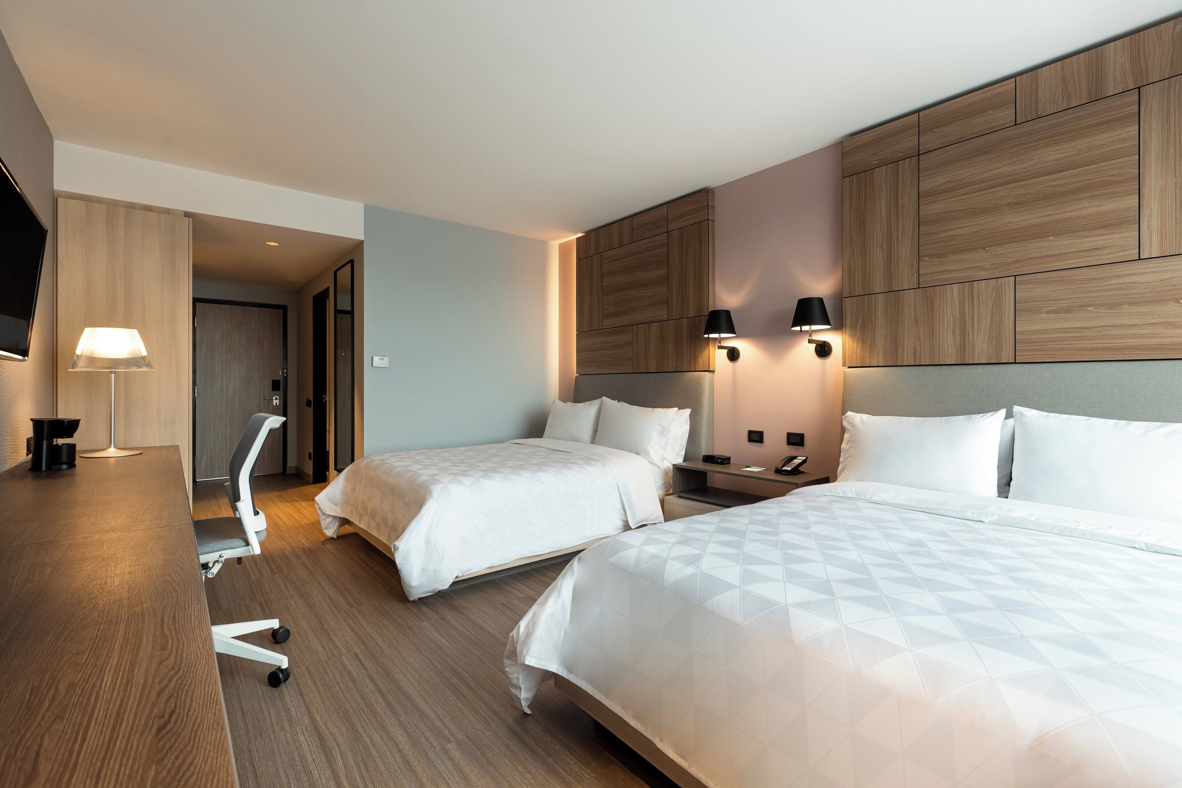 Une chambre d’hôtel avec deux lits, un bureau, une chaise et un téléviseur.