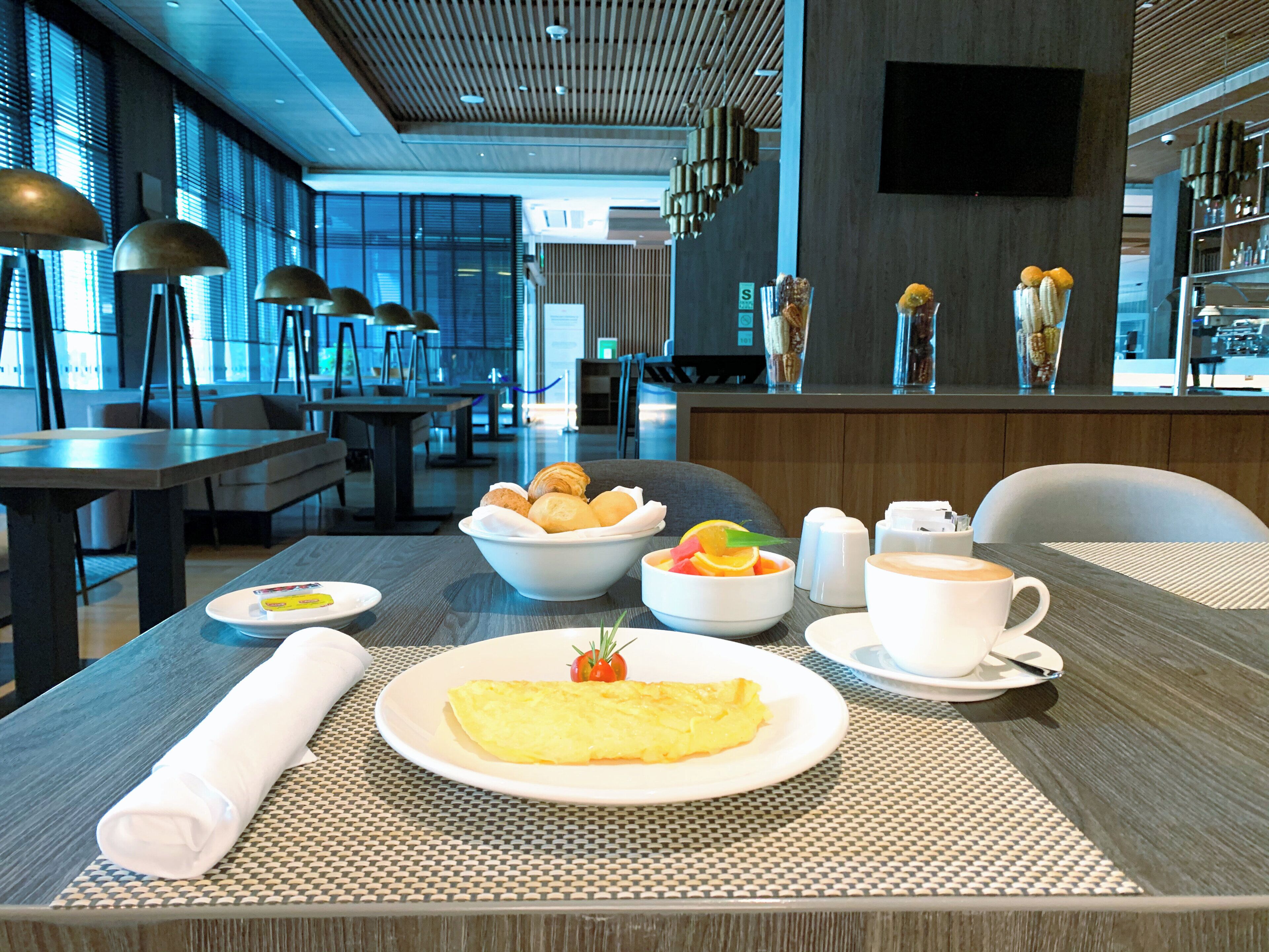 A breakfast setting with a table set for two, including plates of food, a rolled towel, and a coffee cup.