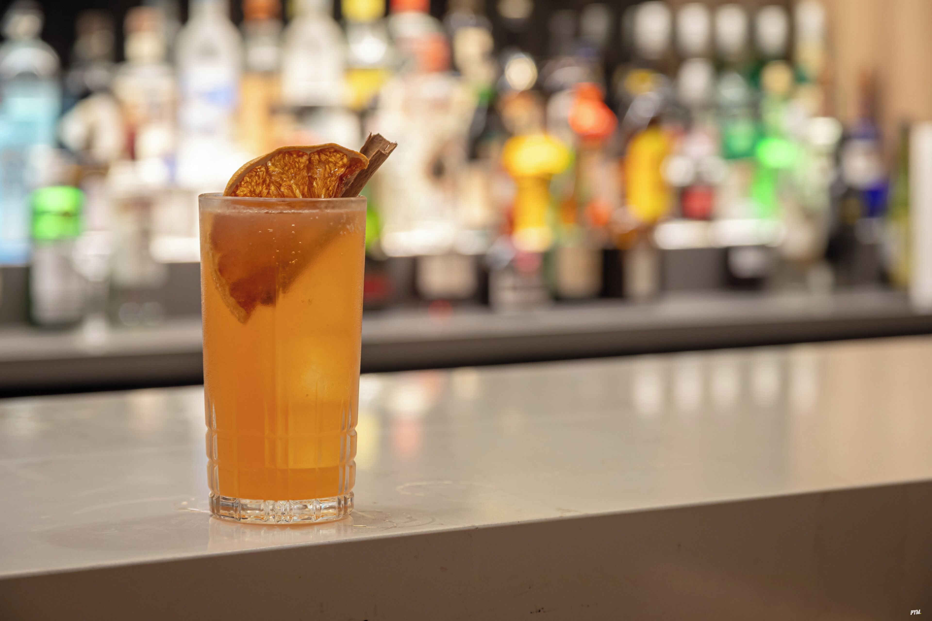 A tall glass with a dried orange slice garnish on a bar counter.