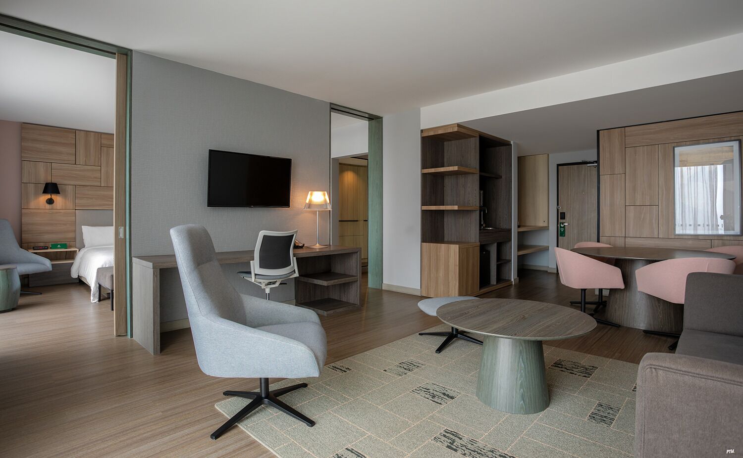 A modern living room with a grey sofa, a round coffee table, a TV mounted on the wall, and a wooden bookshelf.