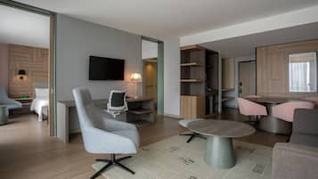 Una sala de estar moderna con un sofá gris, una mesa de centro redonda, un televisor montado en la pared y una estantería de madera.
