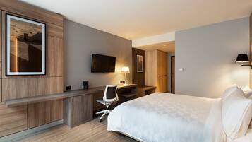 Una habitación de hotel moderna con cama, escritorio, silla y televisor de pantalla plana montado en la pared.