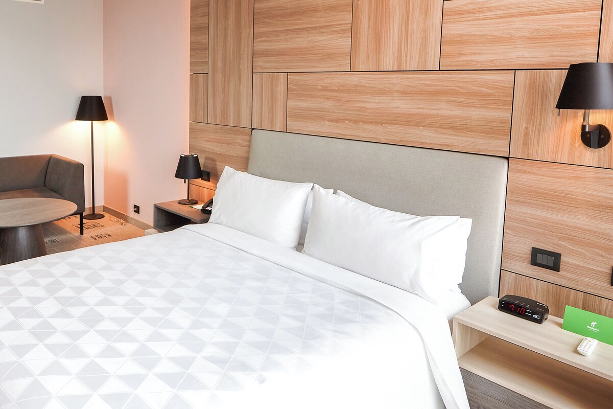 Hotellihuone, jossa on sänky, sohva, pyöreä pöytä ja yöpöytä, jossa on lamppu.