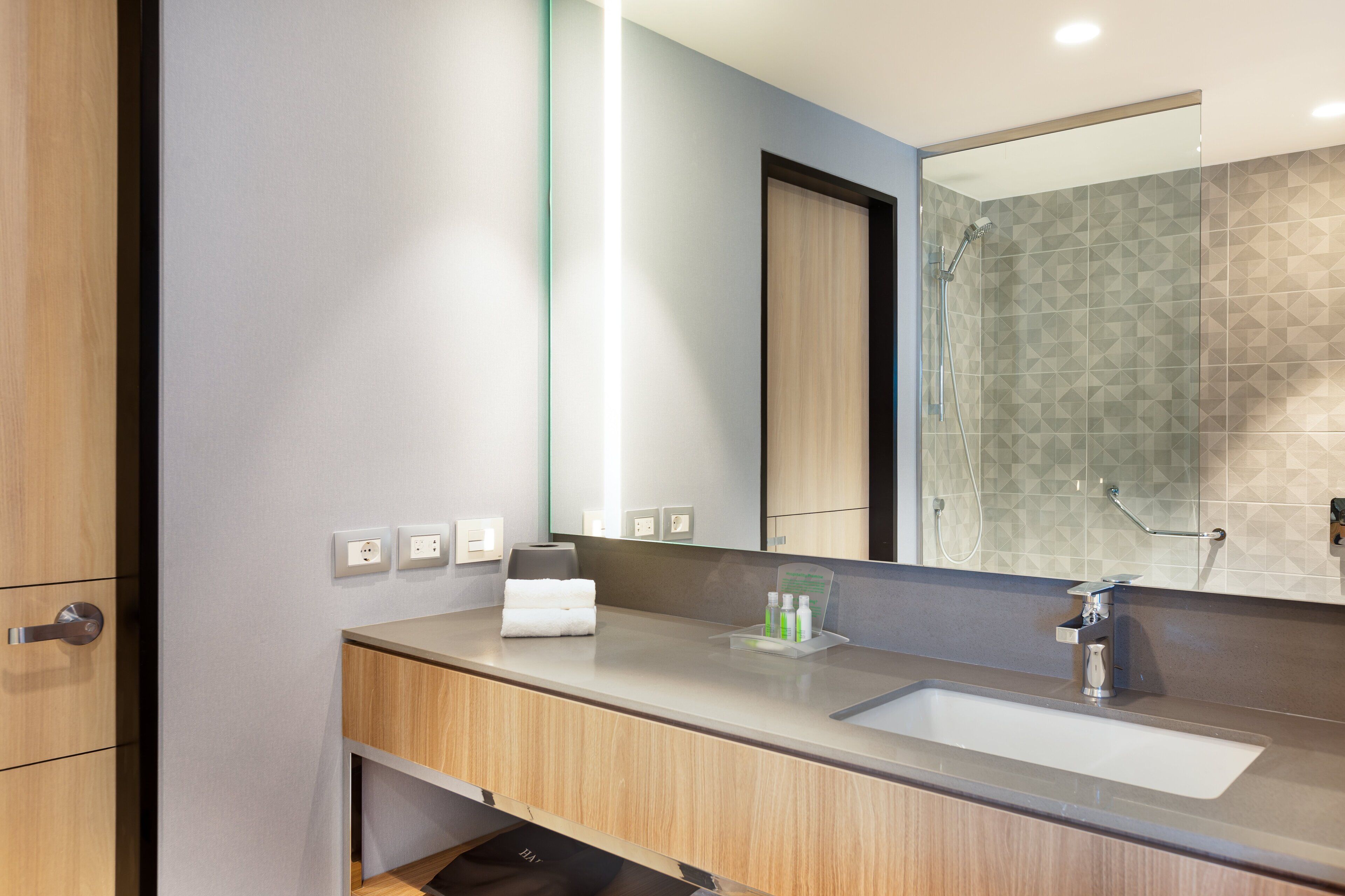 Une salle de bain moderne avec un meuble-lavabo en bois, un grand miroir et un espace douche.