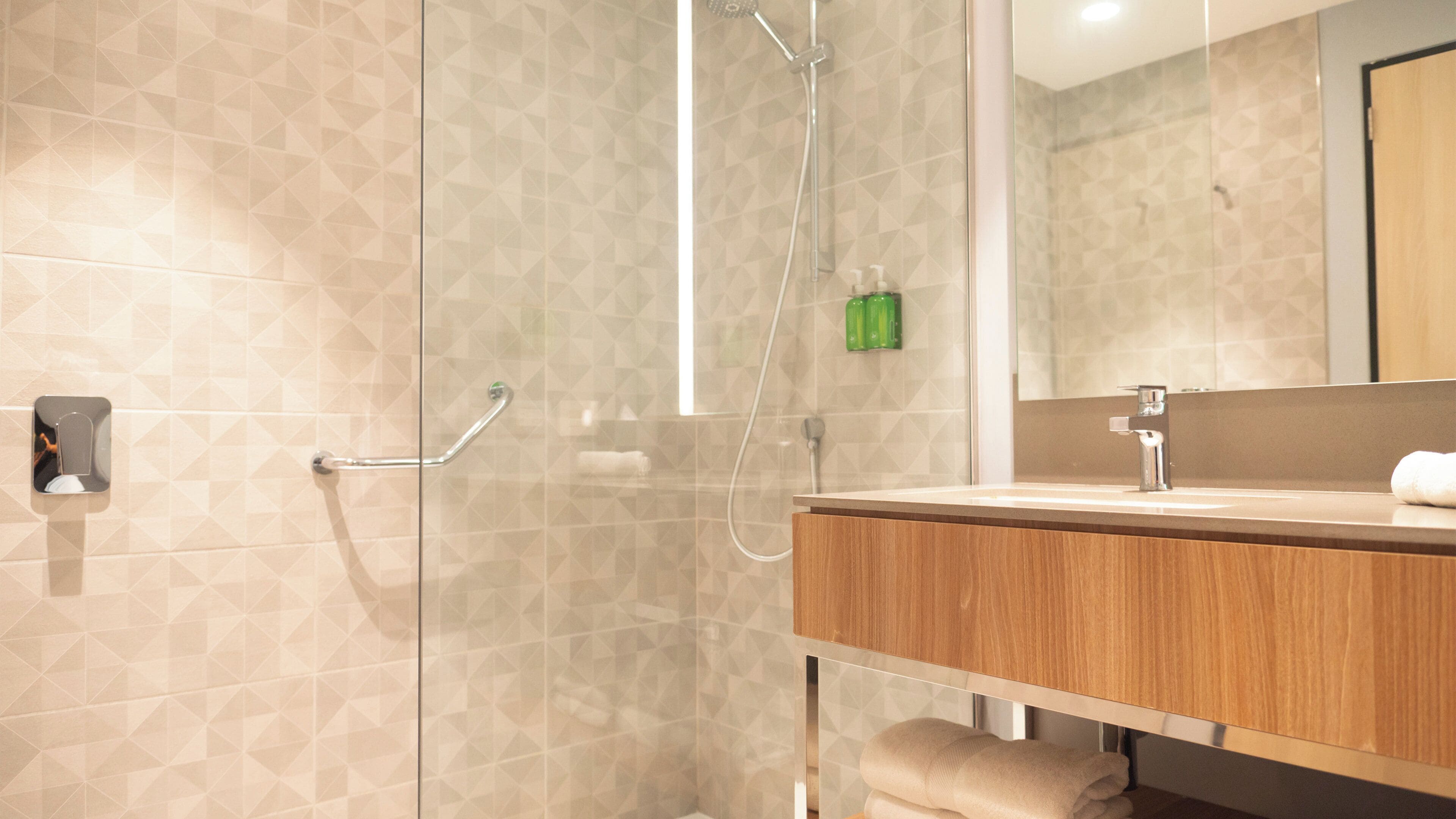 Un baño moderno con cabina de ducha de vidrio, tocador de madera y un espejo.