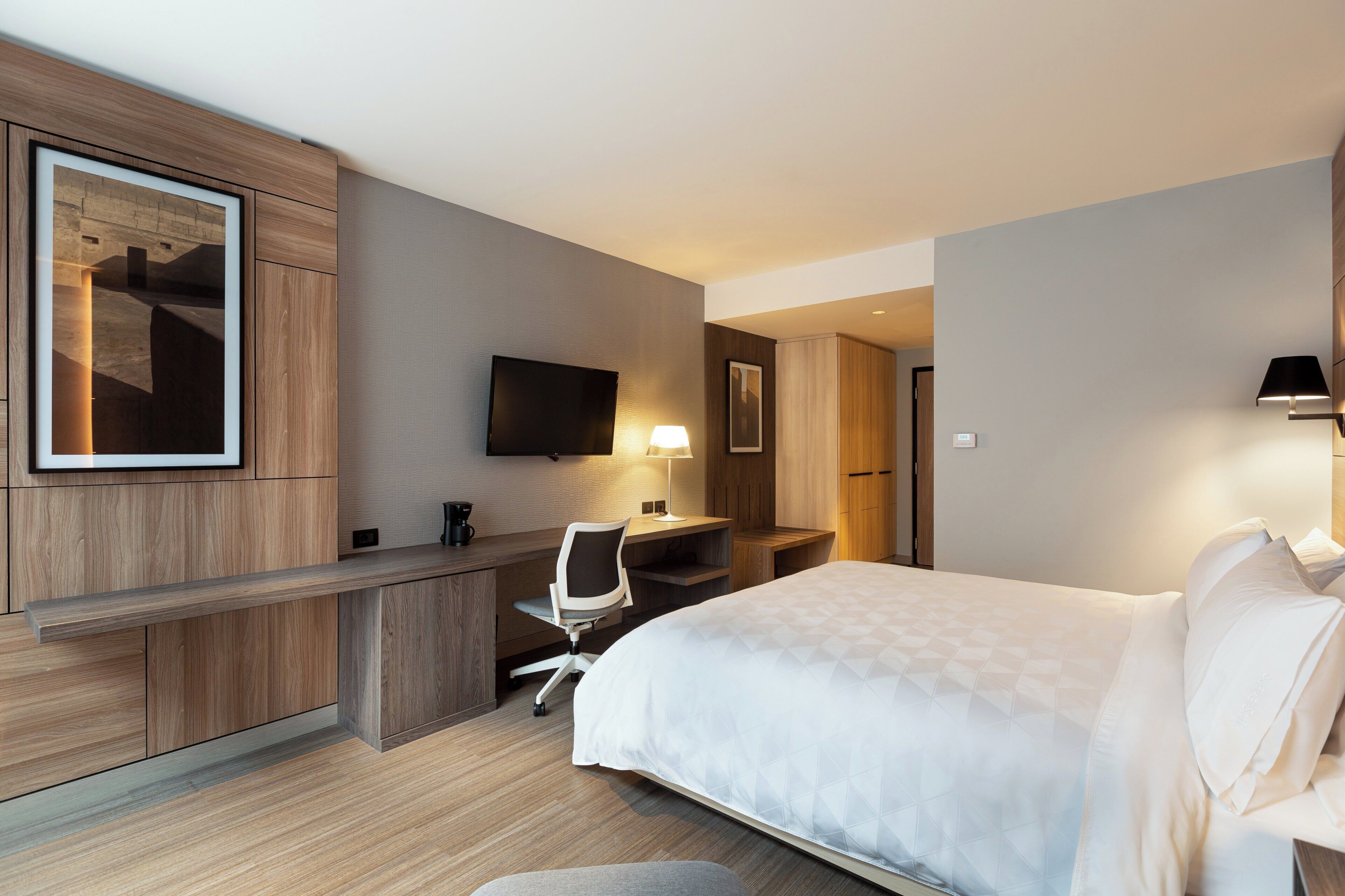 A hotel room with a bed, desk, chair, and a flat-screen TV.