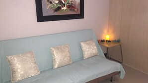 A room with a light blue sofa, three patterned cushions, a framed abstract painting, and a small table with a candle and decorative items. - Staycation at smdc grass residences (Quezon city)