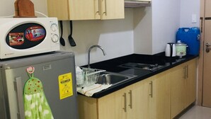 A compact kitchen with wooden cabinets, a refrigerator with a green towel, a microwave, a sink, and a blue water container. - Staycation at smdc grass residences (Quezon city)