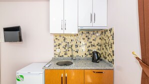 Een kleine keuken met witte kastjes, een ingebouwde magnetron, een spoelbak met betegelde spatwand en een waterkoker.
