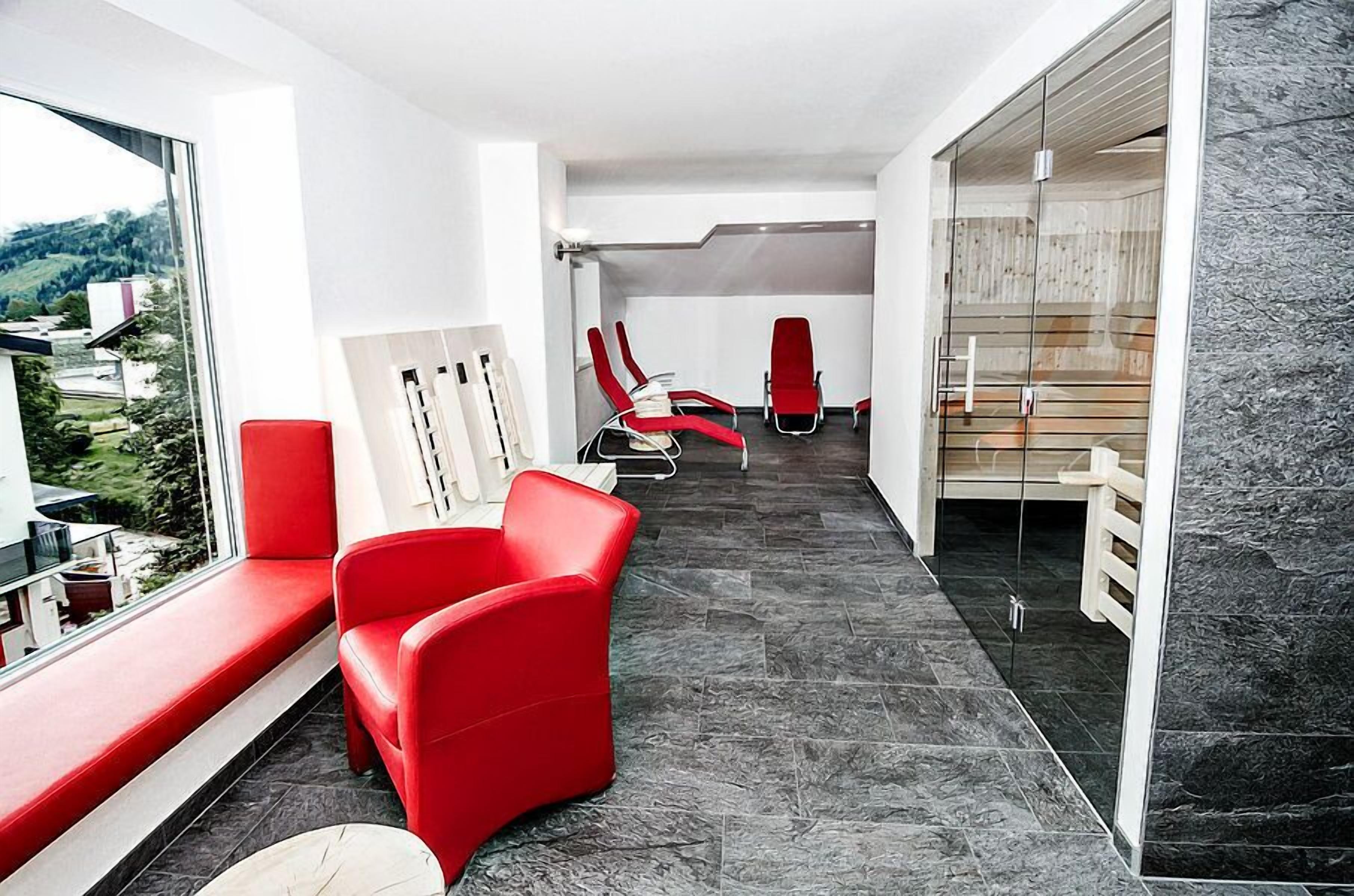 Ein modernes Hotelzimmer mit einem roten Sofa, einer Glasdusche und Blick ins Freie.