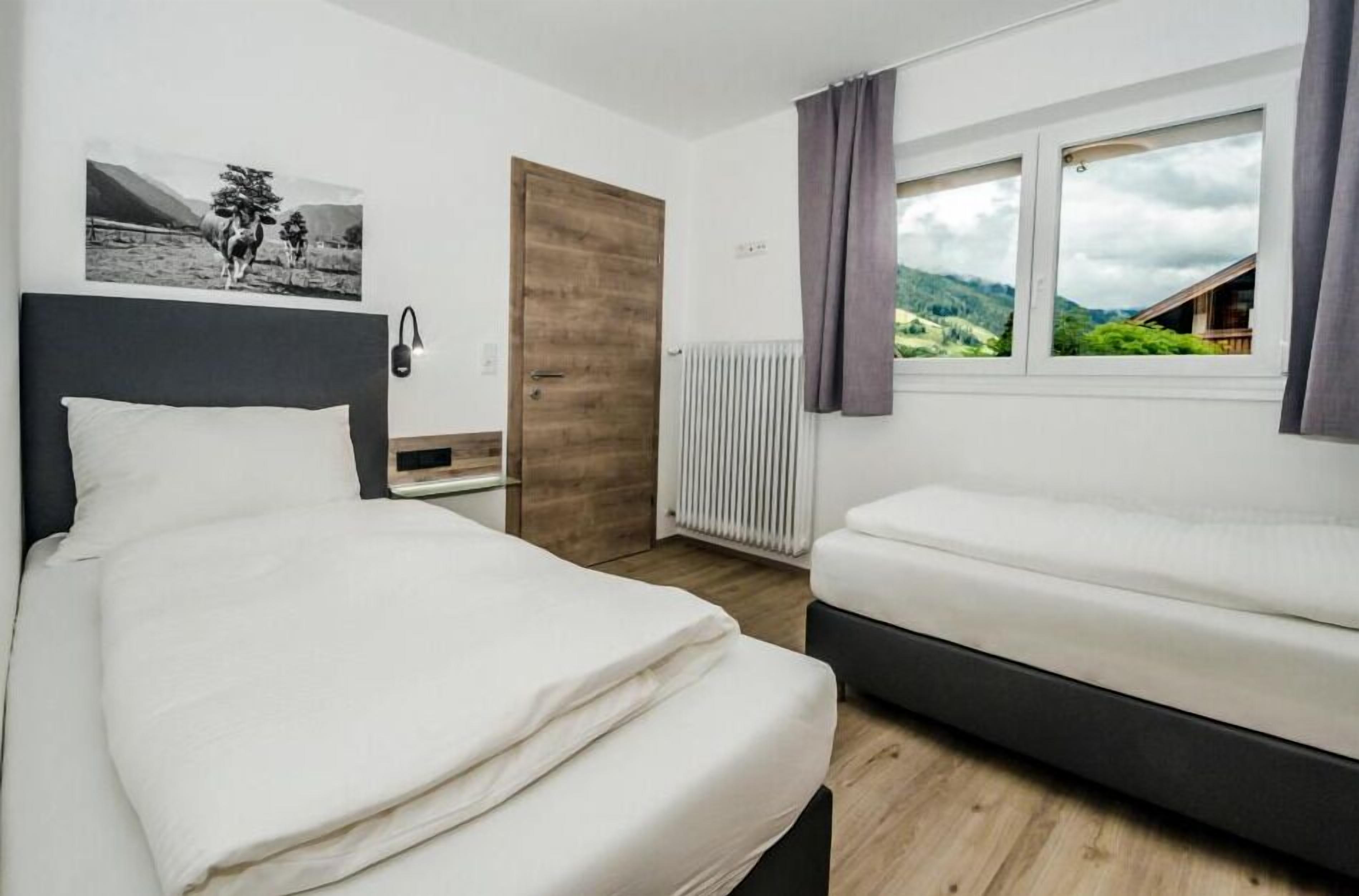 Ein Zimmer mit einem Bett, einer Couch, einem Fenster mit Vorhängen, einem Heizkörper und einer Tür.
