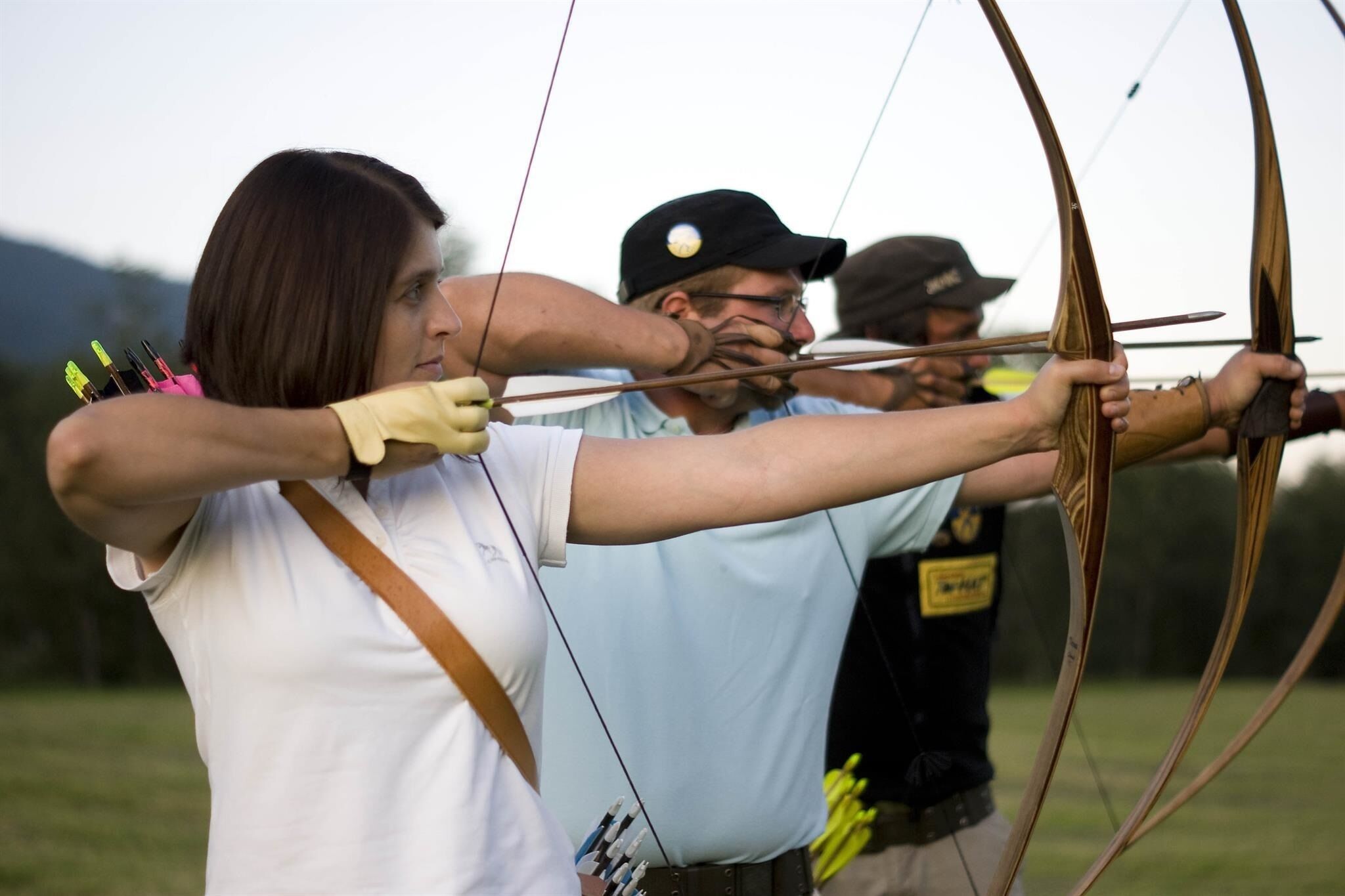 A person aiming a bow with arrows in a field.