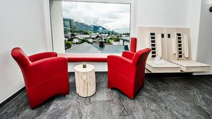 Una habitación moderna con un gran ventanal, dos sillas rojas, una mesita de madera y una camilla de masaje con toallas.