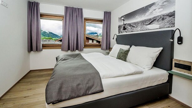 Un dormitorio moderno con una cama, vistas de montañas a través de la ventana y un cuadro en la pared.