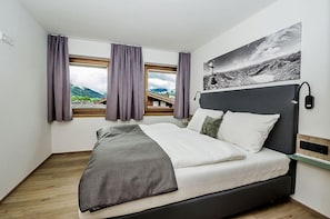 Un dormitorio moderno con una cama, vistas de montañas a través de la ventana y un cuadro en la pared.